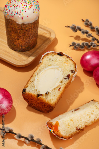 Traditional Easter sweet bread Paska slice spread with creamy butter, served with pink dyed eggs on a peach background