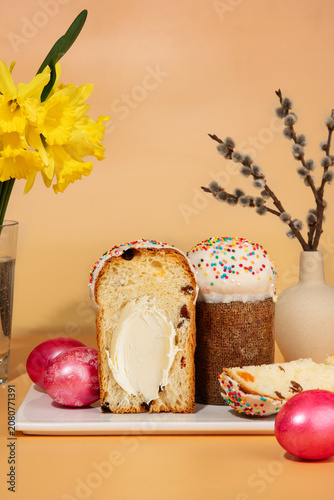 Traditional Easter sweet bread Paska slice spread with creamy butter, served with pink dyed eggs on a peach background