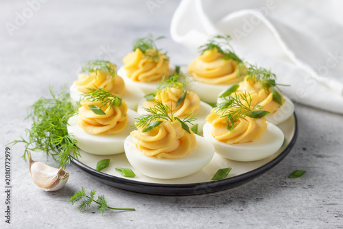 Boiled eggs stuffed with garlic and mayonnaise filling, garnished with fresh dill and green onion. Protein rich appetizer served on a plate, close up view