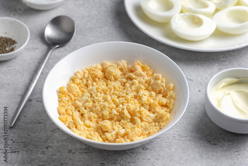 Crumbled hard boiled egg yolks in a bowl, garlic, mayonnaise and seasonings, prepared as filling for stuffed eggs on a gray textured surface