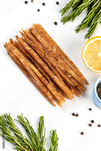 Dried fish sticks snack served on a round wooden cutting board with sea salt crystals, bright background