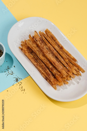Dried fish sticks snack served on a round wooden cutting board with sea salt crystals, bright background