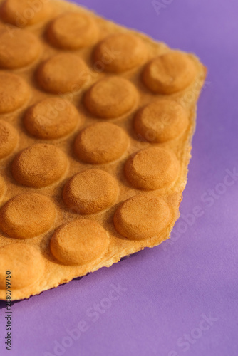 Close-up of a golden Hong Kong bubble waffle base on a vibrant purple background.