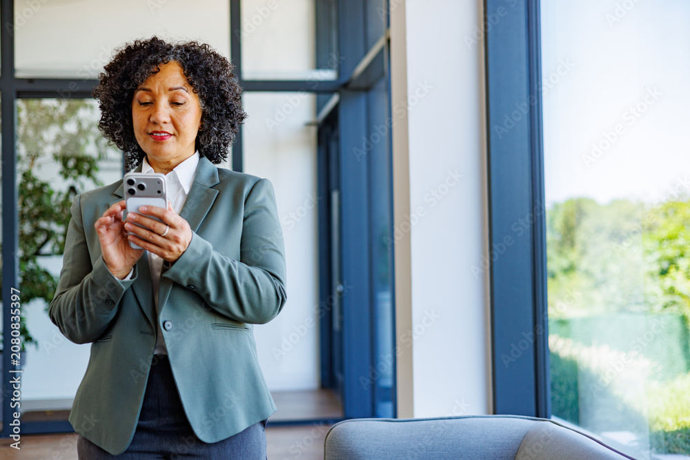 Fototapeta premium Professional mature businesswoman using a smartphone, connecting and communicating in a modern office environment
