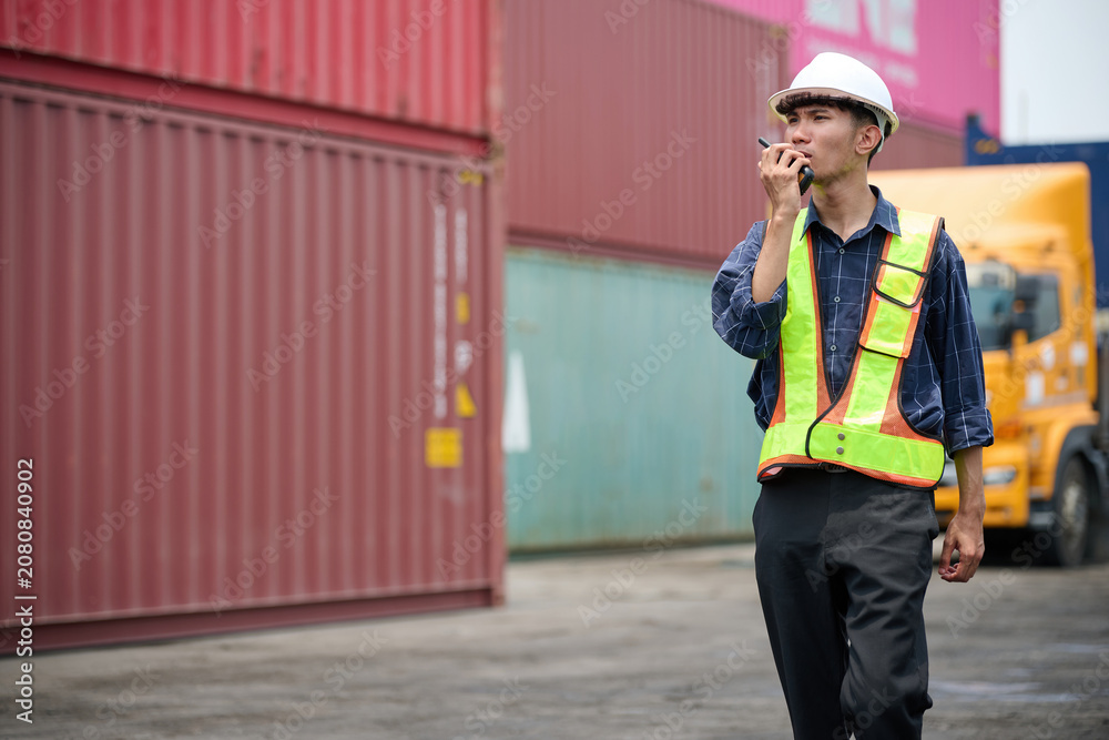 Fototapeta premium Warehouse worker using walkie talkie to communicate during the work shift in the cargo containers area