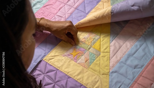 Close-up view of a person's hands meticulously stitching together colorful fabric layers to create a geometric quilt pattern.