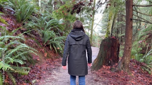 Woman walking on forest trail in Vancouver rainforest, back view with rain jacket