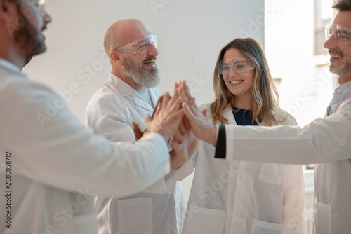 Jubilant Research Team Celebrates Scientific Discovery with Group High-Five in Bright Laboratory 