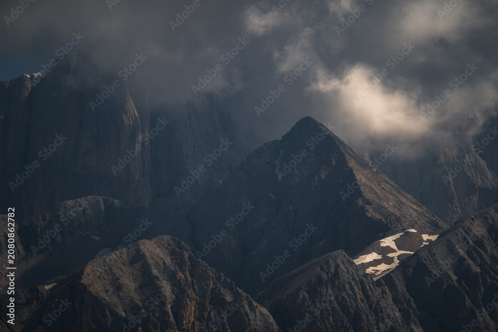 Fototapeta premium Dramatic and atmospheric mountain landscape featuring jagged peaks under heavy, moody clouds. Perfect for travel, nature, and adventure-themed backgrounds.