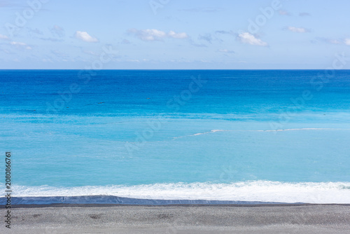 Pacific Ocean seascape in Taiwan. Clear turquoise water meets the blue horizon. Calm waves crash on a dark pebble beach.