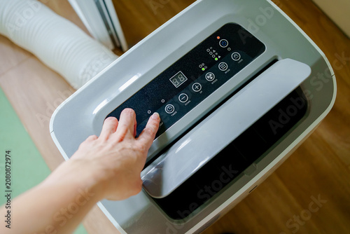 A close-up view of a person's hand pressing a button on the digital control panel of a portable air conditioner unit to adjust the room temperature.