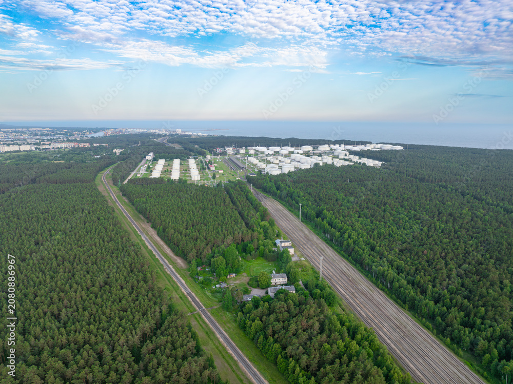 Naklejka premium Aerial view of Ventspils oil storage terminals, railway corridor, pine forest and Baltic Sea coastline in Latvia