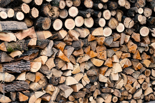 Neatly stacked firewood logs forming a natural wood background. Chopped timber prepared for winter heating, renewable energy and rustic lifestyle.