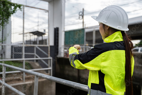 Professional female environmental engineer holding a clipboard inspecting wastewater drainage infrastructure at an industrial facility ensuring safety and sustainable public water management.