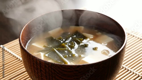 Steaming Bowl Of Miso Soup With Tofu And Seaweed In Dark Wooden Bowl On Bamboo Mat