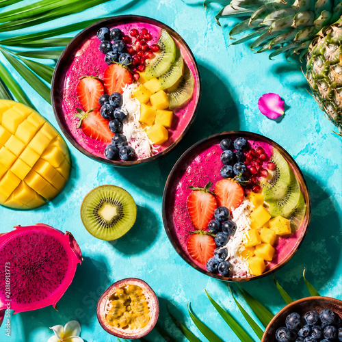 Two tropical smoothie bowls with fresh fruits on blue background