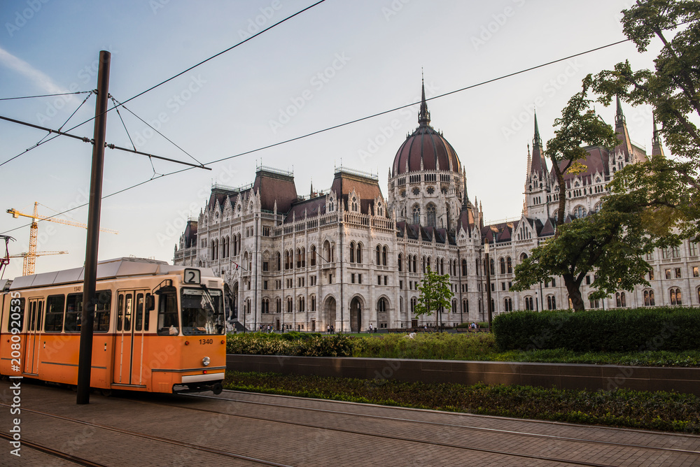Obraz premium Iconic yellow tram moving past the Hungarian Parliament Building in Budapest during golden hour.