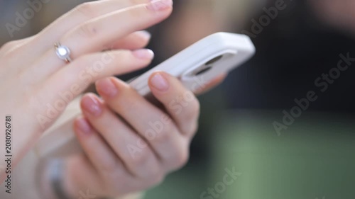 Close-up hands scrolling on white phone. Finger ring glints softly. Soft focus background. Neutral tones. Casual modern gesture