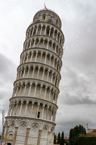 A low-angle view captures the architectural marvel of the Leaning Tower of Pisa, showcasing its unique tilt and detailed facade under an overcast sky