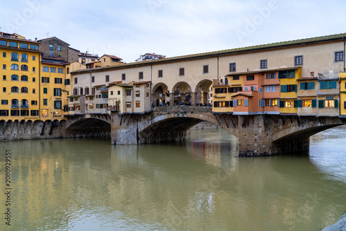 Iconic medieval stone bridge lined with colorful shops and houses spanning the Arno River in Florence, Italy, reflecting in the water