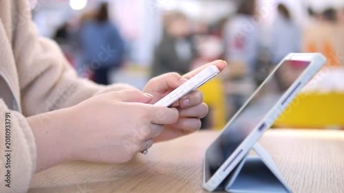 Close-up of hands using smartphone and tablet. Person focused, calm, multitasking in public space. Ideal for tech, education, or digital lifestyle themes. Blurred background suggests busy environment