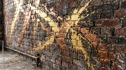 Abstract metallic gold paint splatter on a weathered dark brick wall