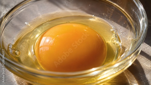 Golden egg yolk in a clear glass bowl on a table