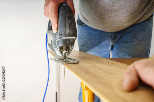Fotografie A front view of a worker using an electric jigsaw tool to cut through a wood laminate flooring plank during a home renovation process
