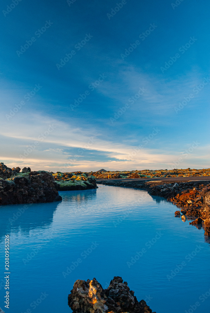 Fototapeta premium Volcanic lava formations beside the Blue Lagoon in Iceland with vivid moss colorful geothermal landscape and crystal blue water