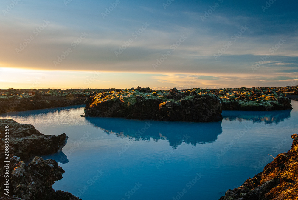 Fototapeta premium Volcanic lava formations beside the Blue Lagoon in Iceland with vivid moss colorful geothermal landscape and crystal blue water