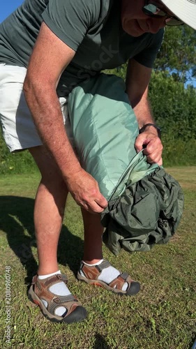 Mature man unpacking and pulling out a green camping tent from its storage carrying bag.
