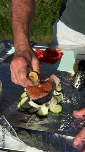 Close up of man squeezing fresh lemon juice over raw fish steak on aluminum foil outdoors.