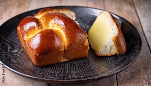 a freshly baked pull apart brioche bread loaf with a glossy golden crust is served on a dark rustic plate with a slice of butter