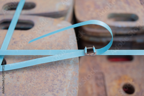 Konstfotografi Heavy rusty iron counterweights secured together with a bright blue plastic stra