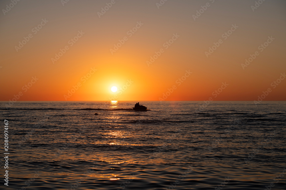 Obraz premium A jet ski sails across the sea at sunset.