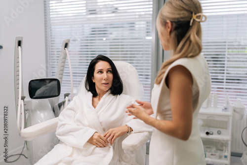 Side view of cosmetologist discussing treatment options with client during a professional consultation at modern beauty clinic, providing expert skincare advice and aesthetic services.