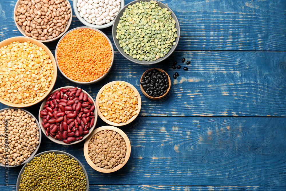 Obraz premium Different types of legumes in bowls on blue wooden table, flat lay. Space for text