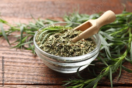 Bild auf Leinwand Dry tarragon in glass bowl, scoop and fresh leaves on wooden table, closeup