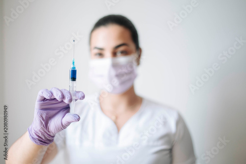 Female healthcare worker presenting a syringe prepared for vaccination or medical treatment in a clinical environment.