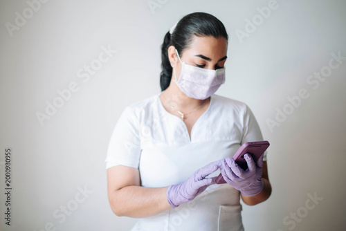 Female nurse wearing protective gloves using a smartphone while working in a modern healthcare environment.