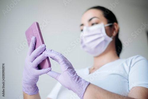 Close-up of a nurse using a smartphone while wearing protective gloves in a professional healthcare environment.