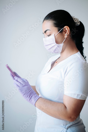 Healthcare professional checking information on a smartphone while wearing protective equipment in a clinical setting.