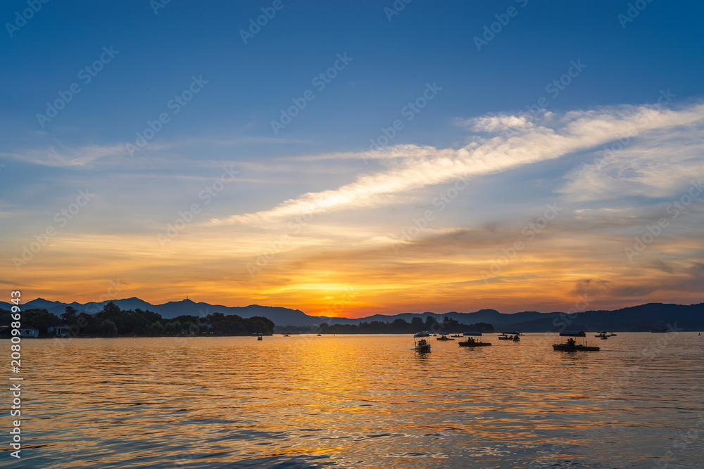 Obraz premium Sunset over calm lake with boats and mountain silhouettes