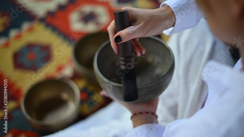 person playing striking and holding tibetan singing bowls on patterned carpet