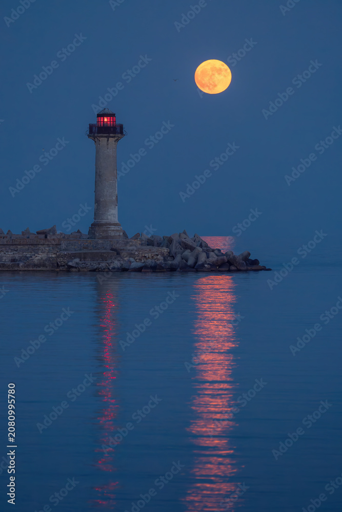 Fototapeta premium Full strawberry moon rising behind Trakata lighthouse near Euxinograd in Varna Bulgaria
