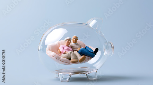 Miniature senior couple figures rest within a clear piggy bank, symbolizing financial security and retirement savings for an older generation on a blue background