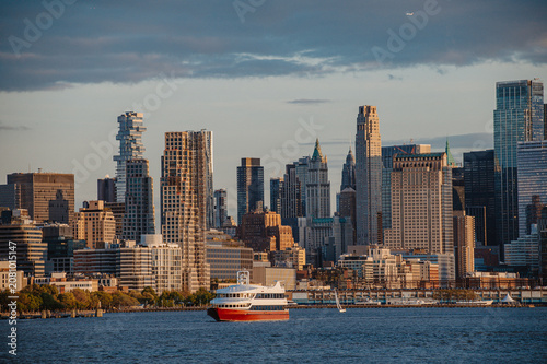 Lower Manhattan skyline with a passenger ferry boat. View of Tribeca skyscrapers including the Jenga tower from the Hudson River during afternoon light.