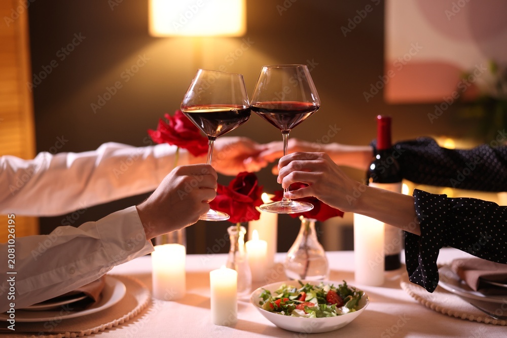 © New Africa - Date. Couple clinking glasses of red wine at table indoors, closeup
