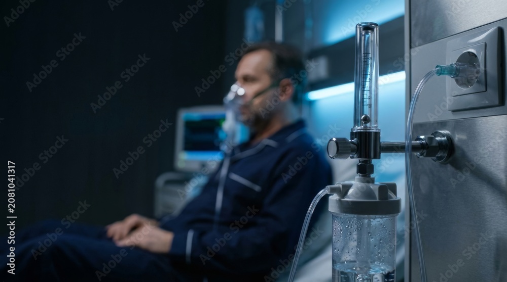Fototapeta premium A male patient wearing an oxygen mask rests in a hospital bed at night. Medical equipment for therapy in a healthcare facility.