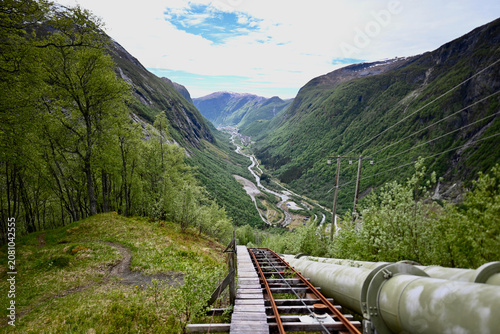 View from a staircase and industrial pipe down to the valley of Dale, Norway, on a sunny summer day with mountains and colorful Nordic scenery.